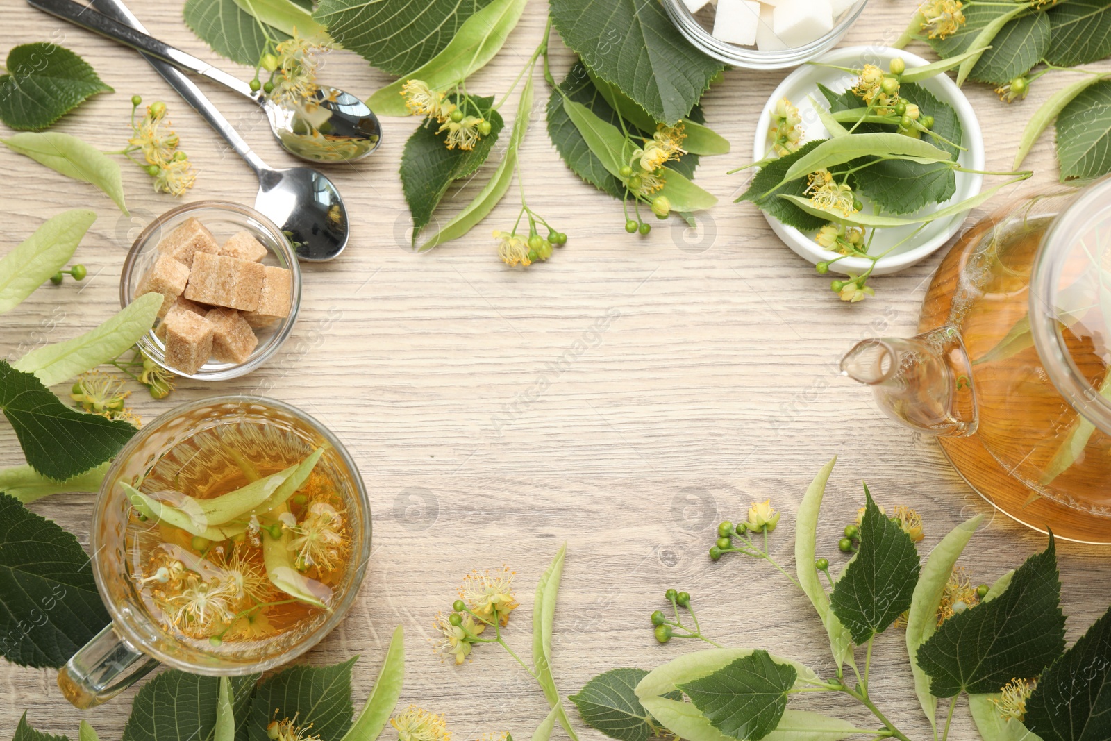 Frame made of fresh linden tea in cup, teapot, sugar cubes and flowers on wooden table, flat lay. Space for text Photo of Frame made of fresh linden tea in cup, teapot, sugar cubes and flowers on wooden table, flat lay. Space for text