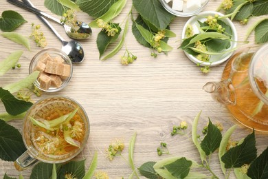 Photo of Frame made of fresh linden tea in cup, teapot, sugar cubes and flowers on wooden table, flat lay. Space for text