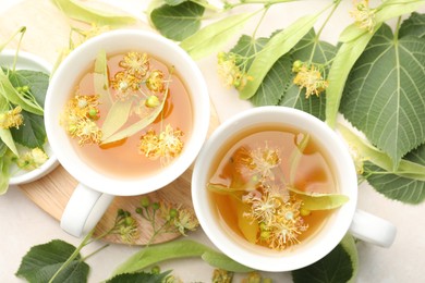 Photo of Fresh linden tea in cups and flowers on white table, flat lay