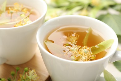 Photo of Fresh linden tea in cups and flowers on white table, closeup