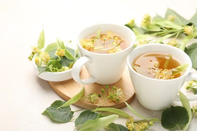 Photo of Fresh linden tea in cups and flowers on white table, closeup