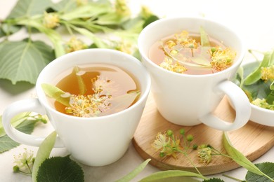 Photo of Fresh linden tea in cups and flowers on white table, closeup