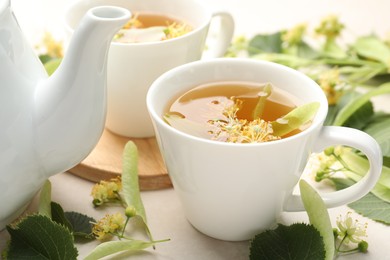 Photo of Fresh linden tea in cups, teapot and flowers on white table, closeup