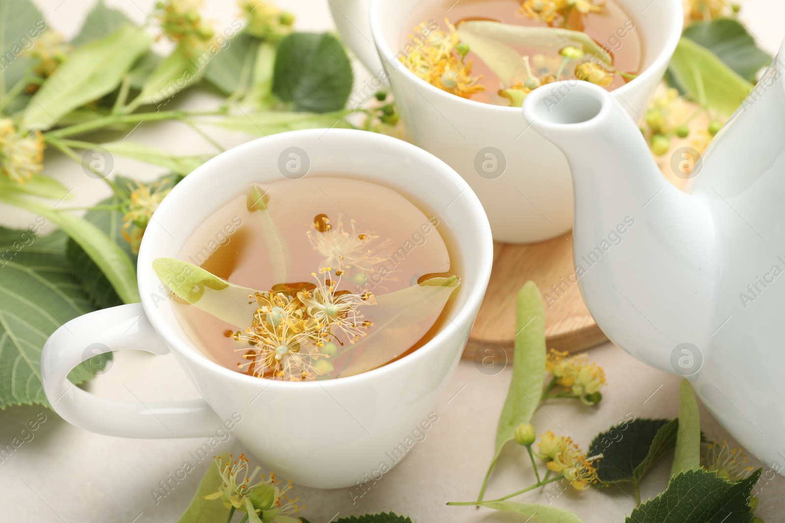 Fresh linden tea in cups, teapot and flowers on white table, closeup Photo of Fresh linden tea in cups, teapot and flowers on white table, closeup