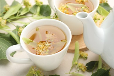 Photo of Fresh linden tea in cups, teapot and flowers on white table, closeup