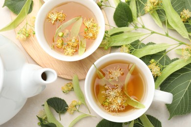 Photo of Fresh linden tea in cups, teapot and flowers on white table, flat lay