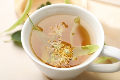 Photo of Fresh linden tea in cup and flowers on white table, closeup
