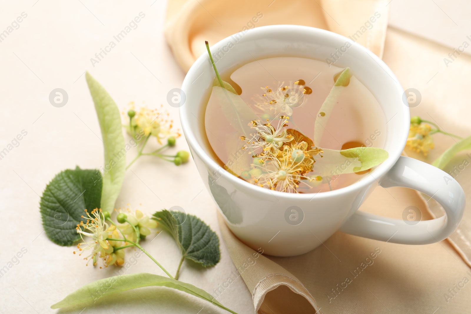 Fresh linden tea in cup and flowers on white table, closeup Photo of Fresh linden tea in cup and flowers on white table, closeup