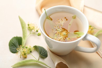 Photo of Fresh linden tea in cup and flowers on white table, closeup