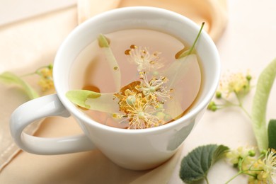 Photo of Fresh linden tea in cup and flowers on white table, closeup