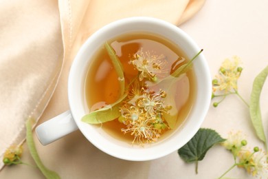 Photo of Fresh linden tea in cup and flowers on white table, flat lay