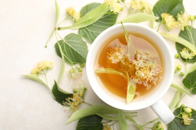 Photo of Fresh linden tea in cup and flowers on white table, flat lay