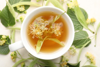 Photo of Fresh linden tea in cup and flowers on white table, flat lay