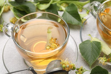 Photo of Fresh linden tea in cups and flowers on light grey table, closeup