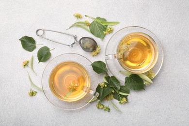 Photo of Fresh linden tea in cups and flowers on light grey table, flat lay