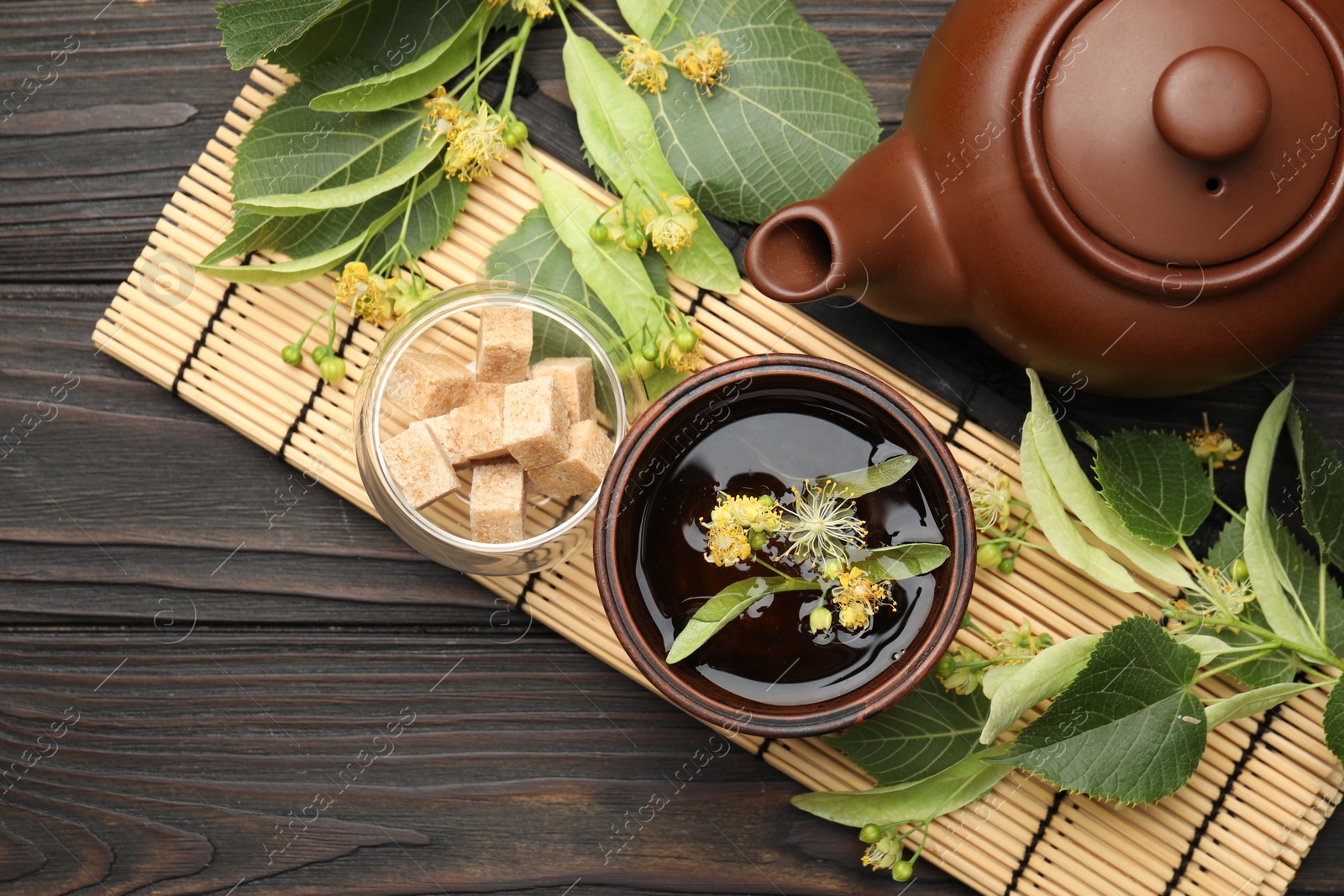 Fresh linden tea in cup, sugar cubes, teapot and flowers on dark wooden table, flat lay. Space for text Photo of Fresh linden tea in cup, sugar cubes, teapot and flowers on dark wooden table, flat lay. Space for text