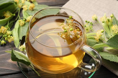 Photo of Fresh linden tea in cup and flowers on dark wooden table, closeup