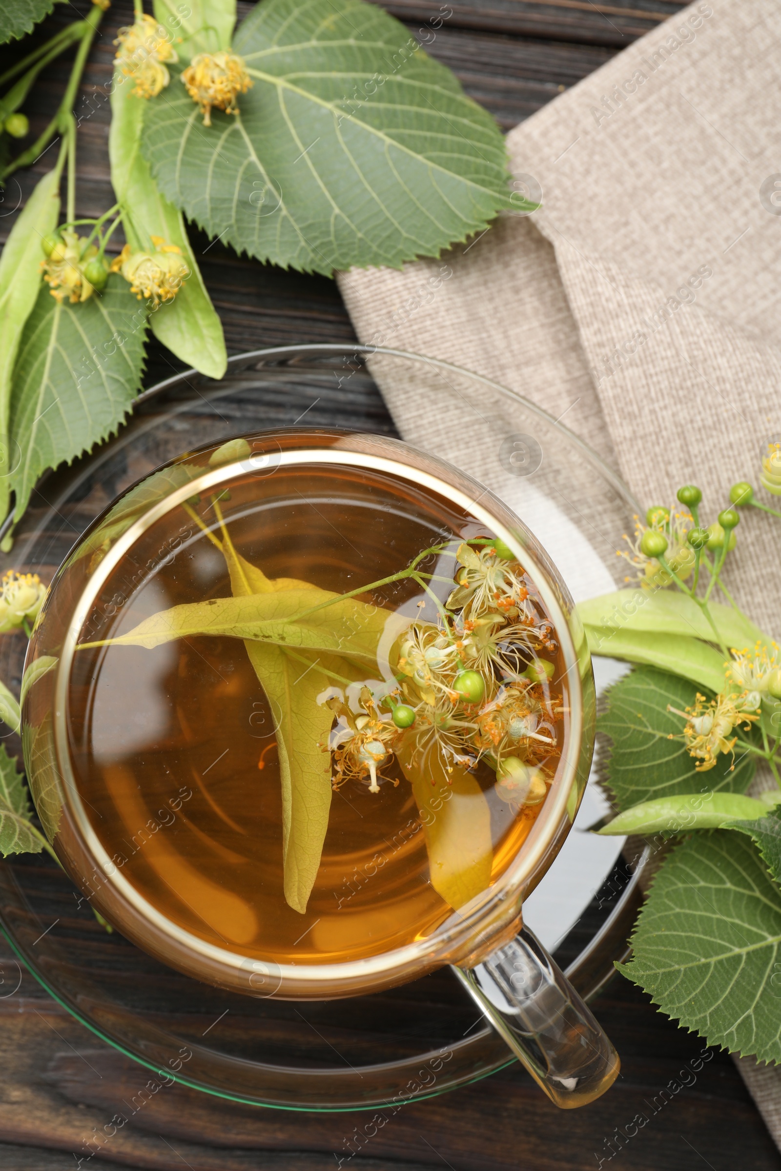 Fresh linden tea in cup and flowers on dark wooden table, flat lay Photo of Fresh linden tea in cup and flowers on dark wooden table, flat lay