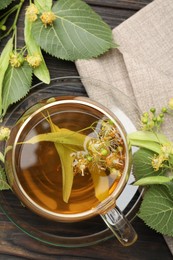 Photo of Fresh linden tea in cup and flowers on dark wooden table, flat lay