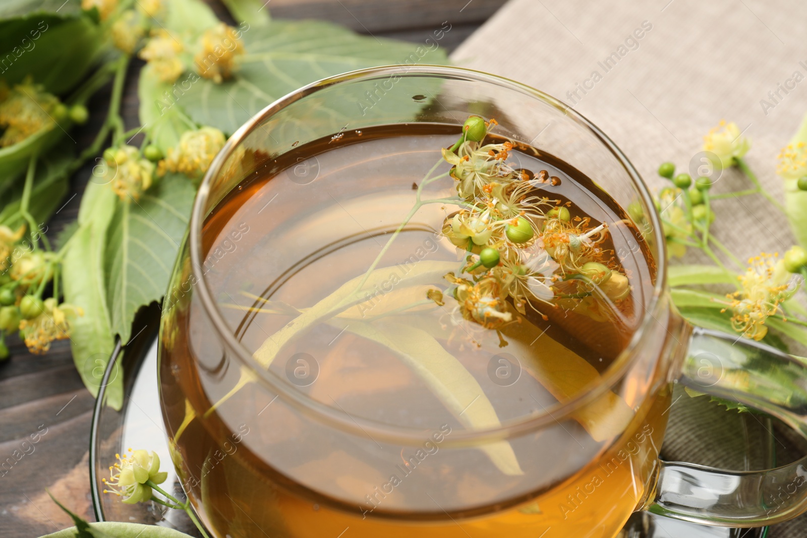 Fresh linden tea in cup and flowers on dark wooden table, closeup Photo of Fresh linden tea in cup and flowers on dark wooden table, closeup