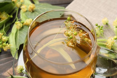 Photo of Fresh linden tea in cup and flowers on dark wooden table, closeup