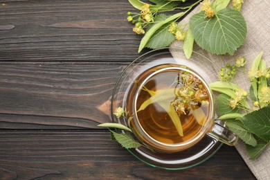 Photo of Fresh linden tea in cup and flowers on dark wooden table, flat lay. Space for text