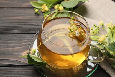 Photo of Fresh linden tea in cup and flowers on dark wooden table, closeup