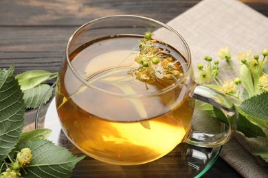 Photo of Fresh linden tea in cup and flowers on dark wooden table, closeup
