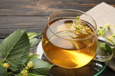 Photo of Fresh linden tea in cup and flowers on dark wooden table, closeup