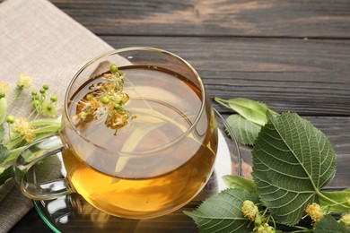 Photo of Fresh linden tea in cup and flowers on dark wooden table, closeup