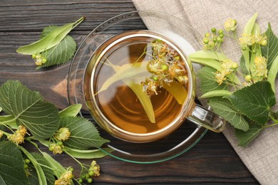 Photo of Fresh linden tea in cup and flowers on dark wooden table, flat lay