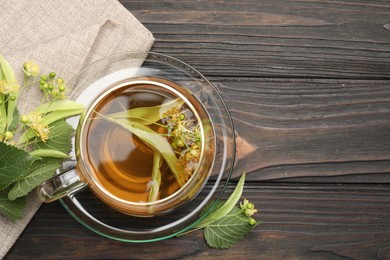 Photo of Fresh linden tea in cup and flowers on dark wooden table, flat lay. Space for text