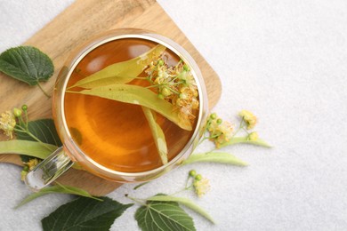 Photo of Fresh linden tea in cup and flowers on light grey table, flat lay. Space for text