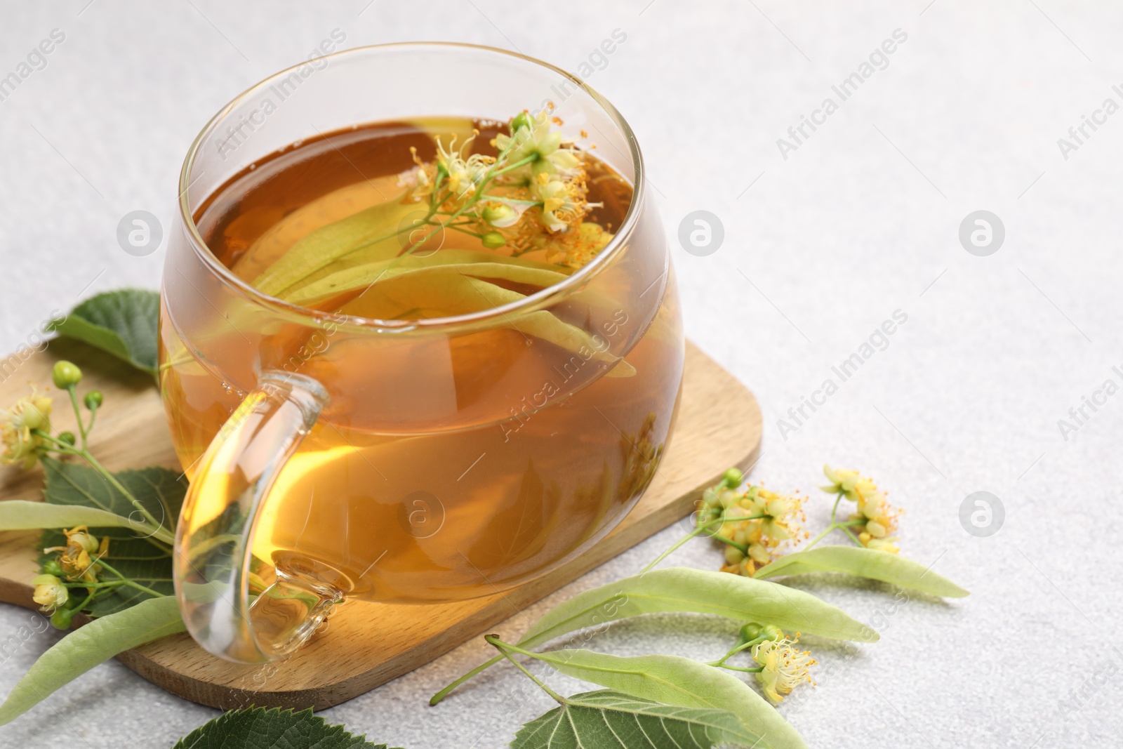 Fresh linden tea in cup and flowers on light grey table, closeup. Space for text Photo of Fresh linden tea in cup and flowers on light grey table, closeup. Space for text