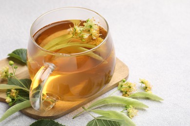 Photo of Fresh linden tea in cup and flowers on light grey table, closeup. Space for text