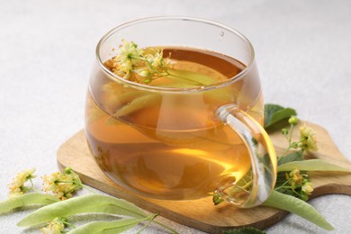 Photo of Fresh linden tea in cup and flowers on light grey table, closeup