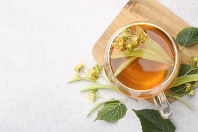 Photo of Fresh linden tea in cup and flowers on light grey table, flat lay. Space for text