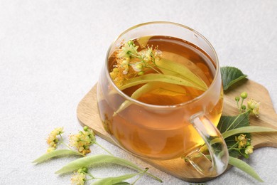 Photo of Fresh linden tea in cup and flowers on light grey table, closeup. Space for text