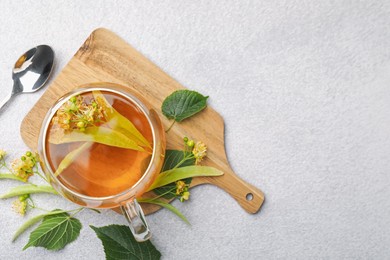 Photo of Fresh linden tea in cup and flowers on light grey table, flat lay. Space for text