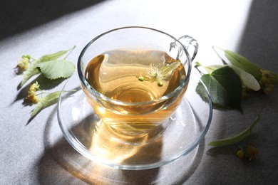 Photo of Fresh linden tea in cup and flowers on light grey table, closeup