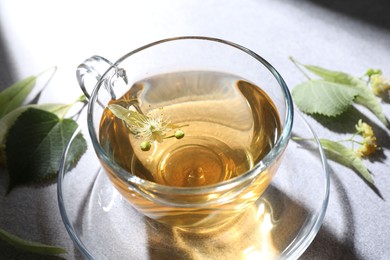 Photo of Fresh linden tea in cup and flowers on light grey table, closeup