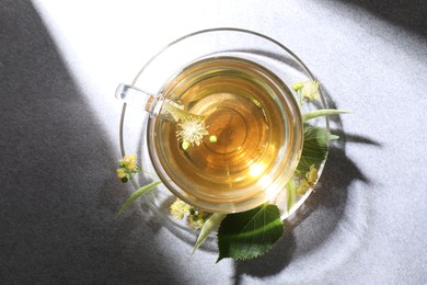 Photo of Fresh linden tea in cup and flowers on light grey table, top view