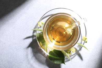 Photo of Fresh linden tea in cup and flowers on light grey table, top view