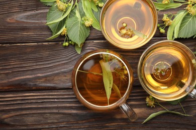 Photo of Fresh linden tea in cups and flowers on wooden table, flat lay. Space for text