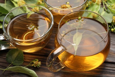 Photo of Fresh linden tea in cups and flowers on wooden table, closeup