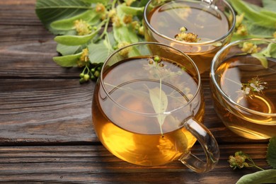 Photo of Fresh linden tea in cups and flowers on wooden table, closeup. Space for text