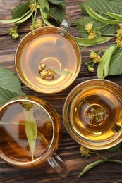 Photo of Fresh linden tea in cups and flowers on wooden table, flat lay