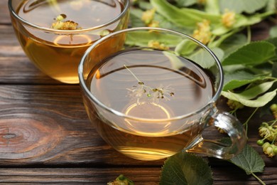 Photo of Fresh linden tea in cups and flowers on wooden table, closeup