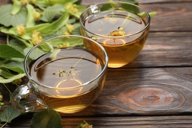 Photo of Fresh linden tea in cups and flowers on wooden table, closeup. Space for text