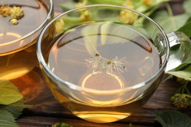 Photo of Fresh linden tea in cups and flowers on wooden table, closeup